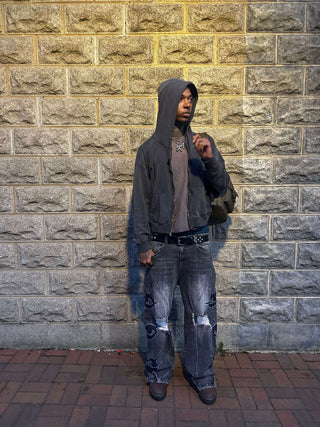 Young man in a hoodie standing against a stone wall, wearing wide leg ripped WYKED denim jeans.